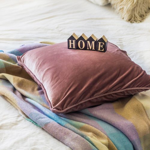 A decorative cozy pillow and the inscription HOME. In the home with a blanket